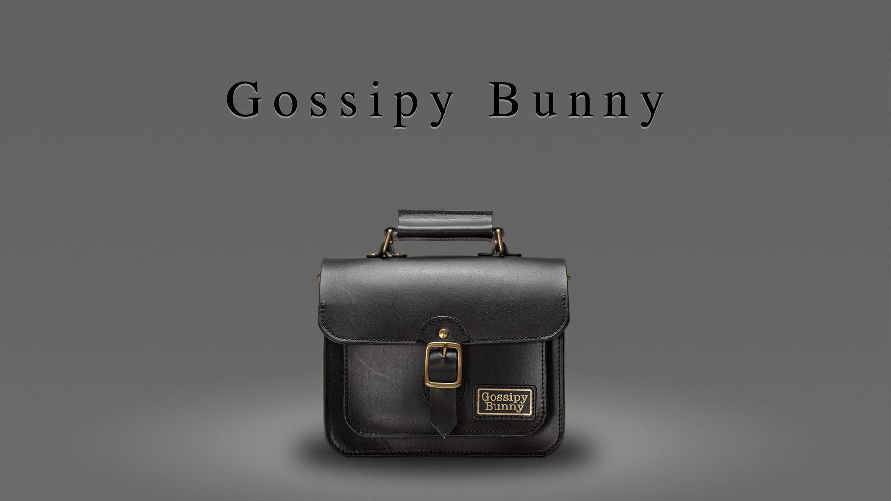 Gossipy Bunny（ゴシッピーバニー）のヒーローバナー画像。黒レザーで仕立てたミニ・サッチェルバッグ〈Shinovy（シノヴィー）〉を上方ライティングで撮影。シネマティックな陰影の中に真鍮パーツの光沢が映える構図で、ブランドの「ビターな革にスパイシーな遊び心」を表現。